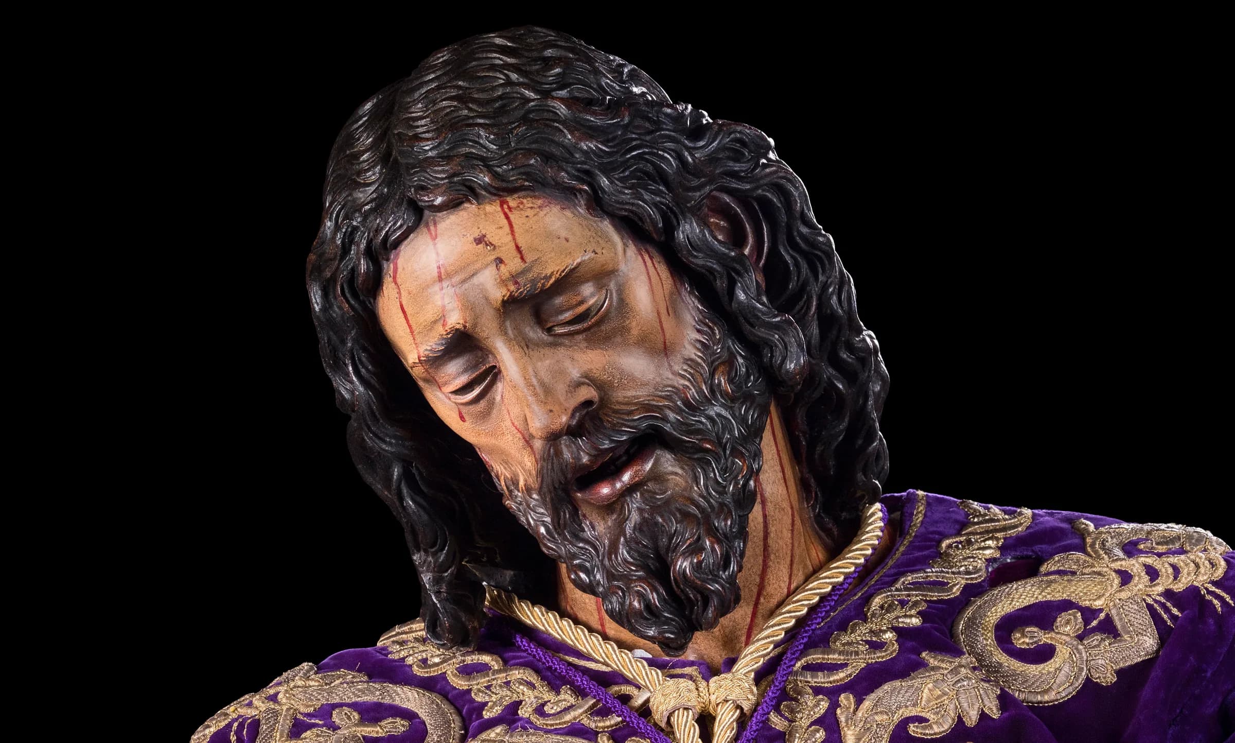 El rostro de Nuestro Padre Jesús de la Pasión, inclinado, con la túnica morada bordada en oro.